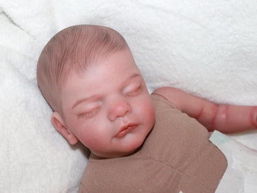 A baby doll peacefully sleeps on a soft white blanket, creating a serene and cozy scene.